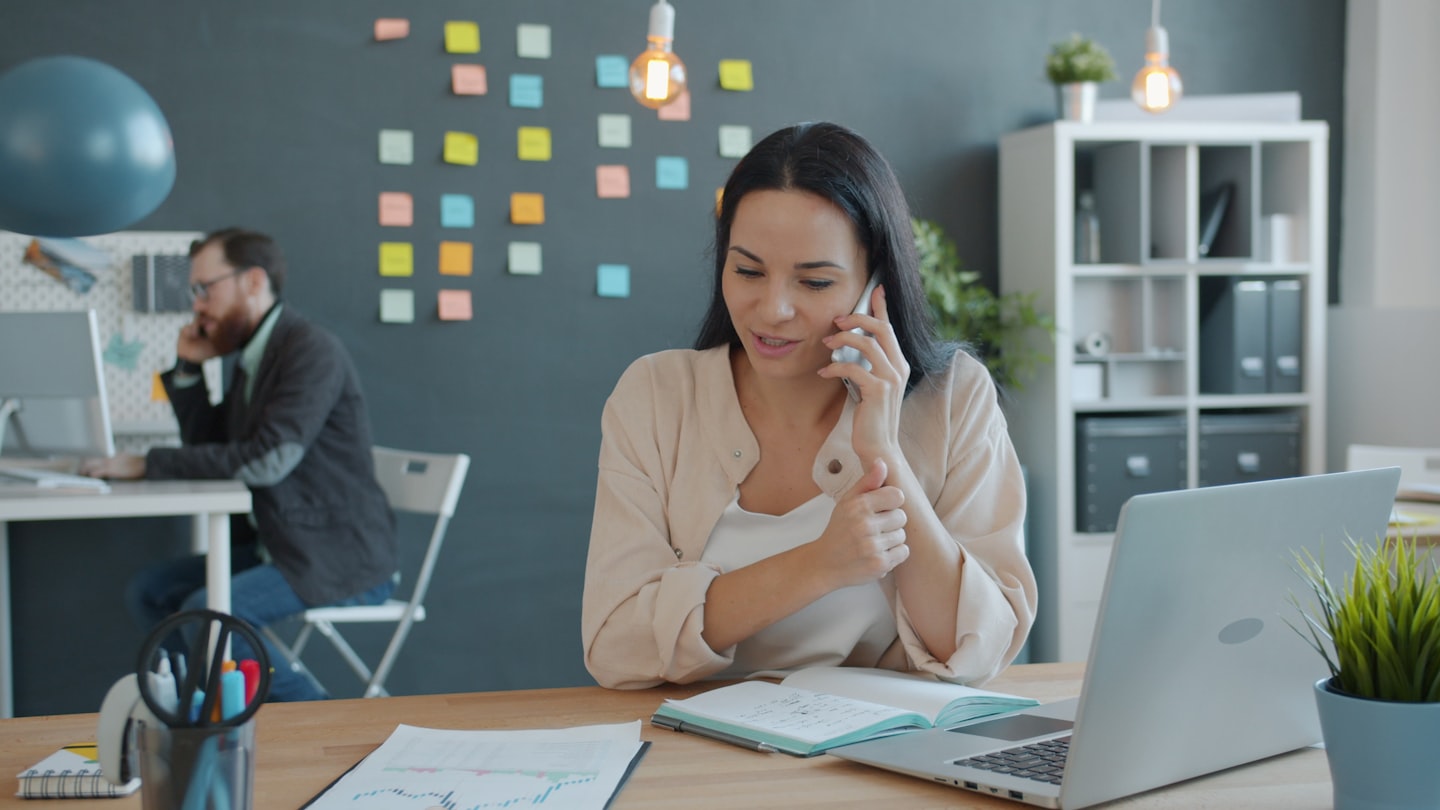 Woman talking on phone at desk with laptop