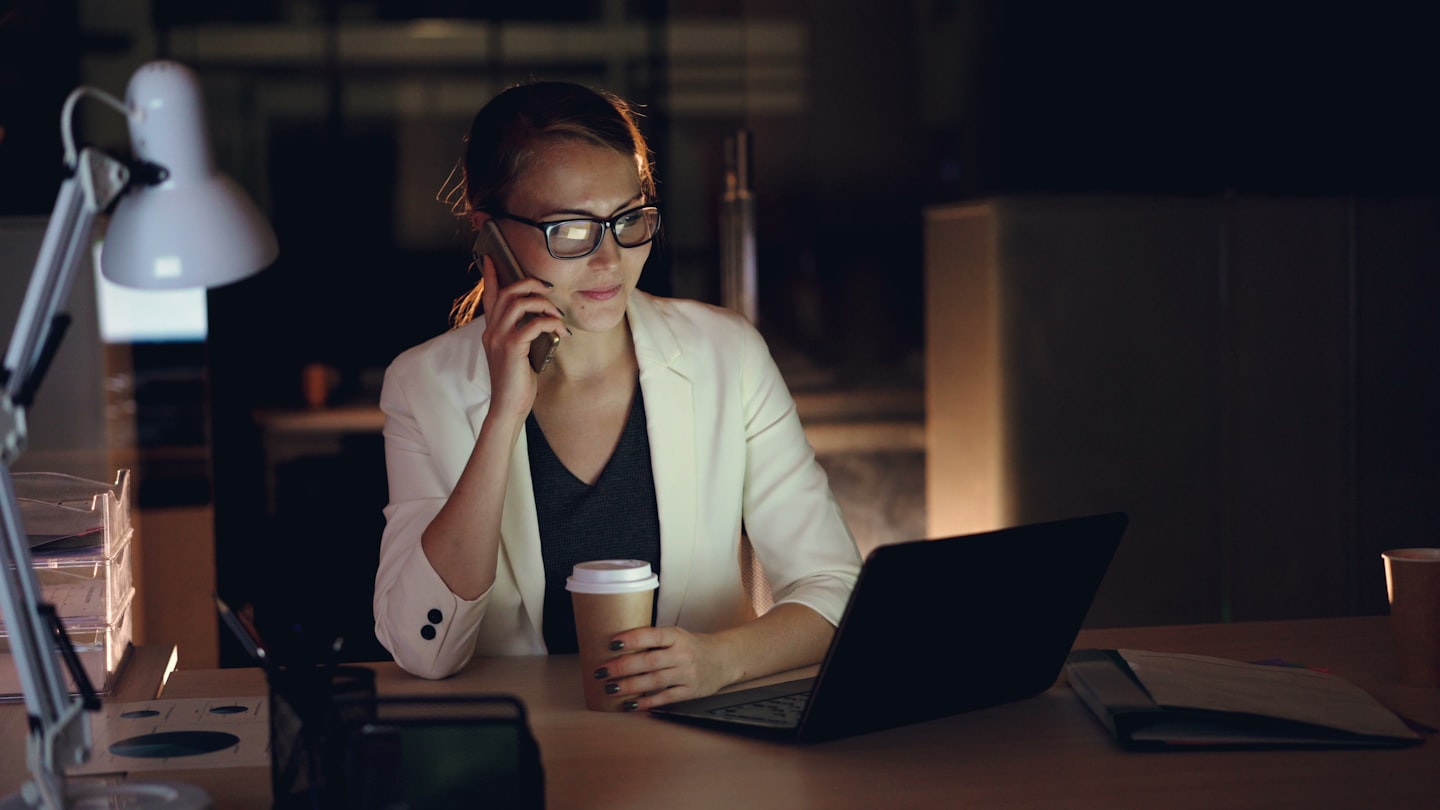 Woman talking on phone at desk with laptop and coffee
