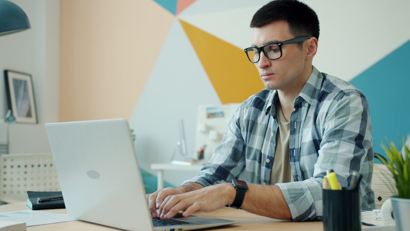 Man wearing glasses types on a laptop at a desk