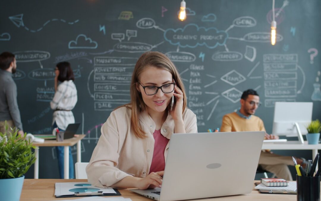 Woman on phone working on laptop in modern office