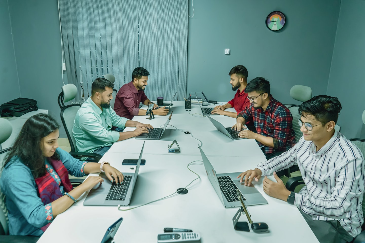 a group of people sitting around a table with laptops